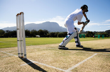 Male cricketer standing in batting crease holding bat facing red ball near stumps, copy space