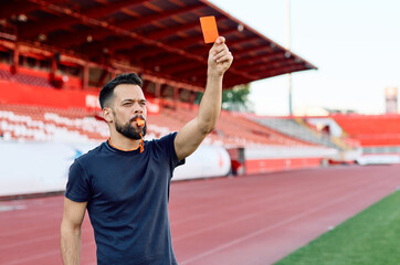 Portrait of a soccer referee blowing a whistle and showing a yellow red card on stadium soccer field