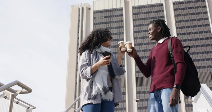 During coffee break Diverse friends on stairs toasting coffee cups checking smartphone descending