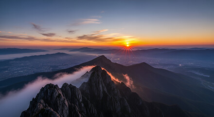 Mountain peaks piercing through the clouds at sunrise with a colorful sky and distant mountain range