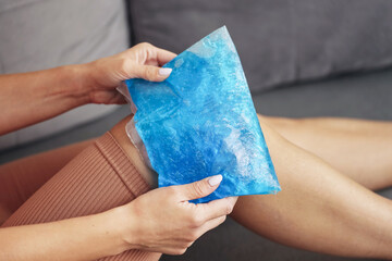 Cold compress on knee. Woman using ice pack for pain relief. Recovery treatment for injury and swelling. Blue gel pack on leg closeup. Health care therapy for muscle strain and joint inflammation.