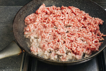 Raw minced meat on frying pan. Cooking ground pork on stove. Fresh food preparation in kitchen. Process of frying meat for meal. Homemade cooking of minced pork dish. Hot pan with sizzling food.