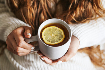 Cup of tea with lemon. Warm drink in woman hands. Relaxing moment with hot beverage. Cozy lifestyle with sweater. Concept of autumn and winter comfort. Morning energy boost. Healthy vitamin drink.