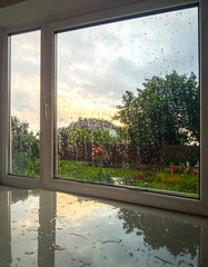 Rainy day view through window; water droplets on glass and sill reflect the outdoors