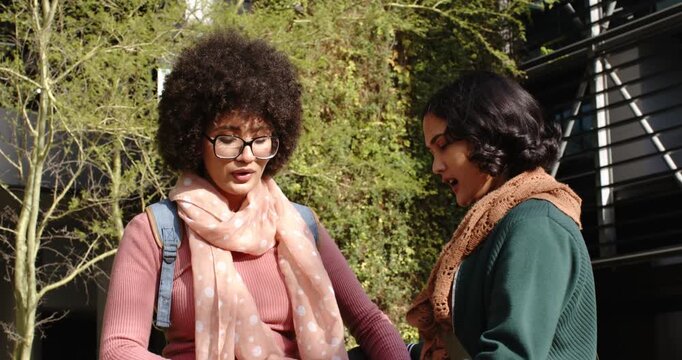 Diverse female friends meeting by scooter on sidewalk preparing it pressing button boarding scooter