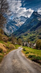 Fototapeta premium A winding gravel road winds through a picturesque valley nestled amongst majestic snow-capped mountains under a vibrant sky.