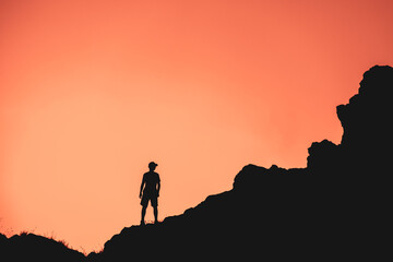 A man stands on a rocky hillside at sunset