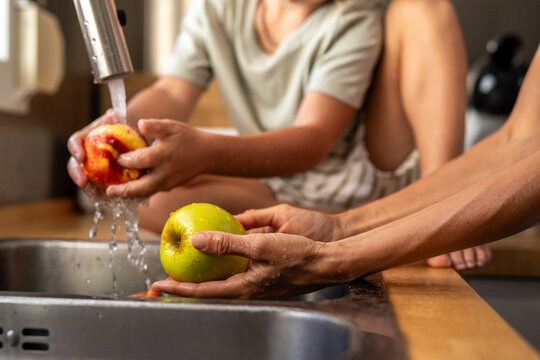 Close-up of child and adult washing fresh apples under running water in the kitchen sink