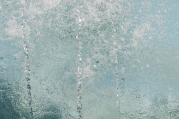 Water droplets burst into the air, reflecting sunlight and creating a cool, refreshing atmosphere around a serene outdoor pool during the day
