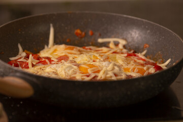 A vibrant frying pan holds colorful shredded vegetables, cheese, and spices cooking together, showcasing the delightful process of food preparation that tantalizes the senses