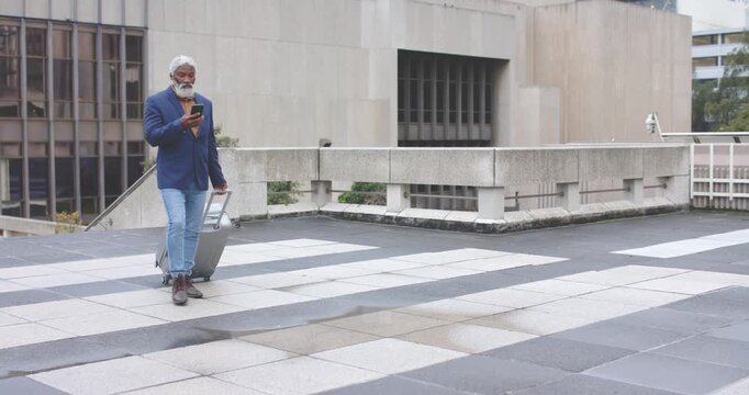 Two mature African American men walking plaza pulling suitcase and checking phones past balustrade