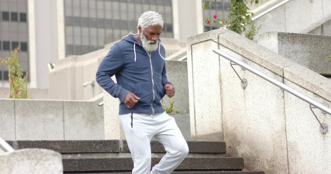 Standing at top of stairs Senior African American man in tracksuit descending then jogging workout