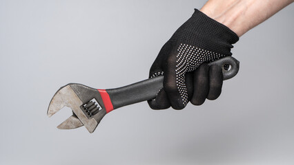 Hand in work glove holding adjustable wrench on gray background