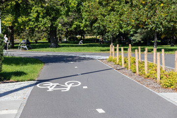 Asphalt bicycle path with white symbol and wooden bollards, bordering green grass in a sunny urban park, promoting active recreation and eco-friendly transport