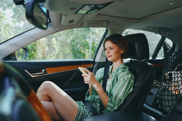 Young woman sits in a modern car, looking at a card or phone, wearing a green striped dress, captured in soft natural light.