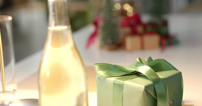 On tabletop, camera shifting focus, showcasing green gift box, snowy trees and glowing pinecone jar