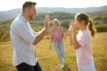 Family enjoys a joyful day outdoors while playing and laughing in a grassy field near rolling hills on a sunny afternoon