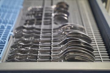 Organized silver spoons in dishwasher cutlery tray with blue dividers for clean kitchen arrangement...