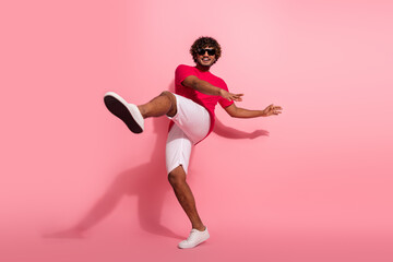 Young man in vibrant casual outfit dancing playfully against a pink studio background
