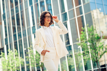 Successful businesswoman in white suit confidently walking outdoors in urban modern city street during sunny day