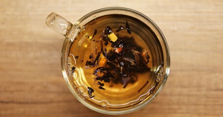 Transparent mug with floral tea and small pieces of lemon on wooden table. Aromatic healthy beverage for breakfast during cold autumn days