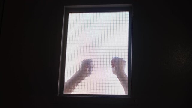 A close-up of a prisoner banging his fist on the window of a pre-trial detention cell