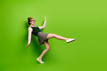 Young woman in school inspired outfit playfully posing against a green background, representing youthful energy
