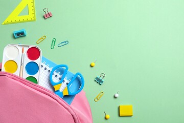 Obraz premium Pink backpack with school supplies on green background. Top view, space for text
