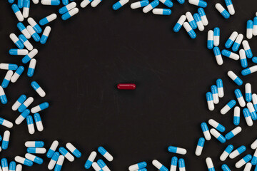 Red pill standing out from the crowd of blue capsules on a black background, a concept of choice, individuality, and unique thinking.