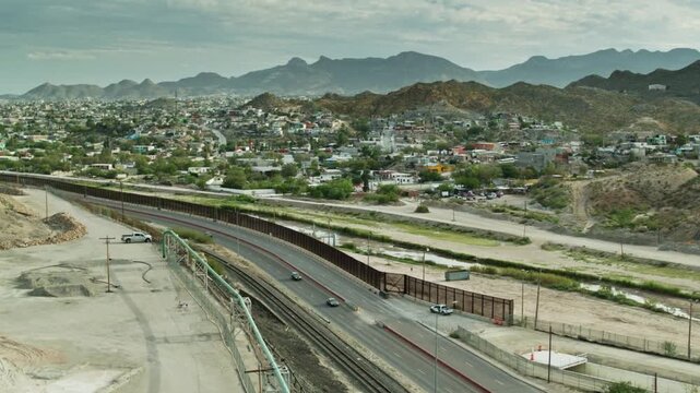 Border fence stretches across the landscape between mountains and city