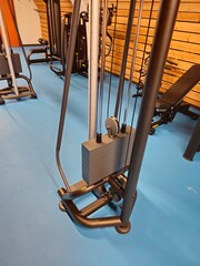 A weight stack from a gym machine shows multiple plates and a yellow adjustment pin, set against a blue floor and wooden wall.