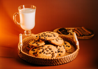 Freshly baked cookies with chocolate chips and a glass of milk on a warm wooden surface