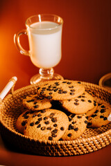 Warm cookies on a woven basket served with a glass of milk in a cozy setting