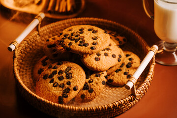 Freshly baked chocolate chip cookies on a woven basket with a glass of milk