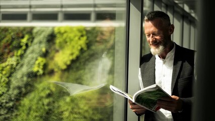 Environmental consultant examining BREEAM sustainability report near window with sunlit green rooftop out of focus behind