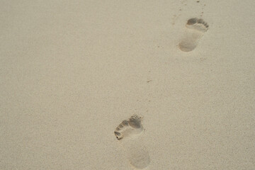 Close-up of two human footprints on smooth beige sand. Minimalist beach scene evoking calm, summer vacation, and natural textures.