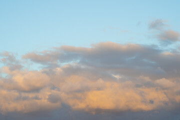 Soft sunset clouds illuminated by warm golden light over blue sky. Peaceful cloudscape background for nature or weather themes.
