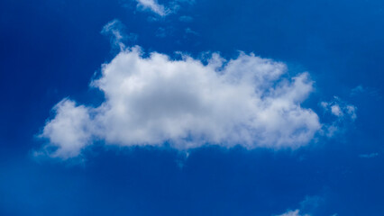 Celestial Puffball: A solitary, fluffy cloud drifts across the boundless azure canvas of the sky,...