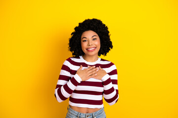 Smiling young woman with striped shirt expressing gratitude against vibrant yellow background
