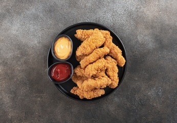 Crispy chicken breast strips with ketchup and cheese sause on a dark background. Top view. Fast food