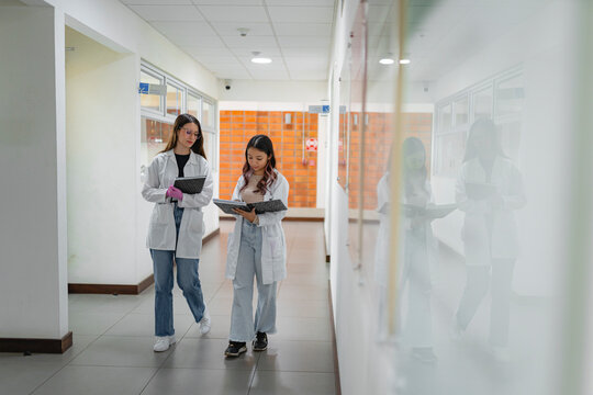 Two female science students walking through university hallway with lab notebooks