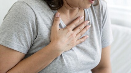 Close Up of Woman in Grey Shirt Clutching Chest in Pain with White Background for Health Concept