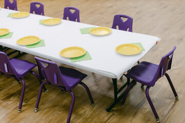 Colorful classroom table set for lunch with yellow plates and green napkins ready for kids