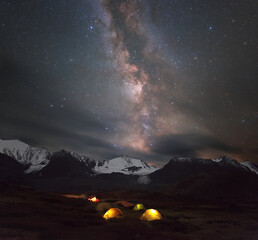 illuminated tourist tents against the backdrop of mountains and the Milky Way.