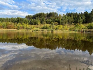 A quiet autumn day, reflection of the forest and clouds in the sky on the water surface