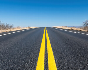 Naklejka premium Lonely road stretching into horizon with vivid yellow centerline under clear blue sky evoking solitude and journey