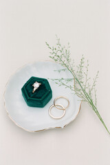 Beautiful engagement ring displayed on a green velvet box beside wedding bands on an elegant plate
