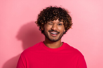 Obraz premium Portrait of a cheerful young man in a red shirt winking confidently against a vibrant pink background