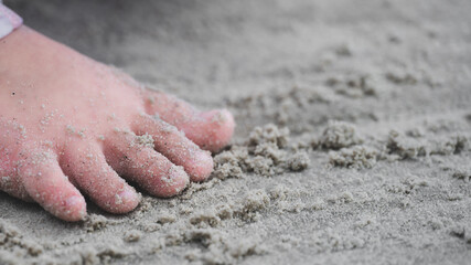 Intimate, detailed close-up of a small child's sandy foot pressing down on fine beach sand. Feeling of being at seaside, childhood freedom, exploration, relaxation, and simple joy of summer a vacation