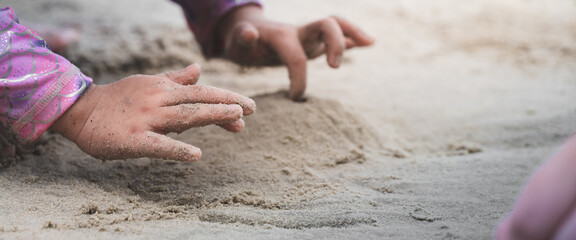 An intimate, close-up, horizontal shot of young child's hands and fingers exploring and digging in soft sand. Child wearing long-sleeved swimsuit top at beach. Childhood freedom and sensory play.